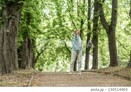 Woman trees park: Person gazes upwards on pathway between trees, summer scene for relaxation. 130514903
