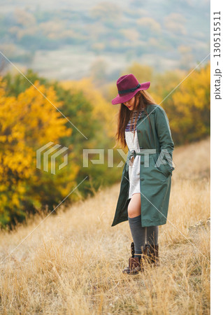 Beautiful stylish girl walks in the autumn park. The girl is dressed in a green coat and a red hat. 130515511