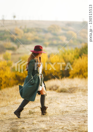 Beautiful stylish girl walks in the autumn park. The girl is dressed in a green coat and a red hat. Beautiful stylish girl walks in the autumn park. The girl is dressed in a green coat and a red hat. 130515513