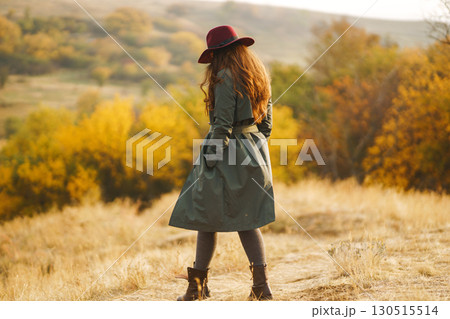 Beautiful stylish girl walks in the autumn park. The girl is dressed in a green coat and a red hat. 130515514