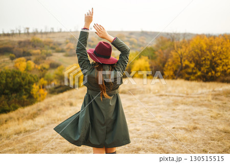 Beautiful stylish girl walks in the autumn park. The girl is dressed in a green coat and a red hat. 130515515