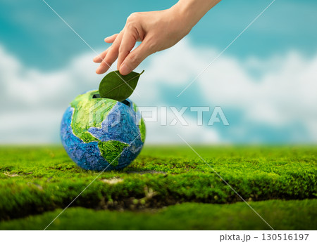 Hand drops a Green Leaf into Globe shaped piggy bank, Eco savings, Green investment, Tree planting and Sustainability concept 130516197