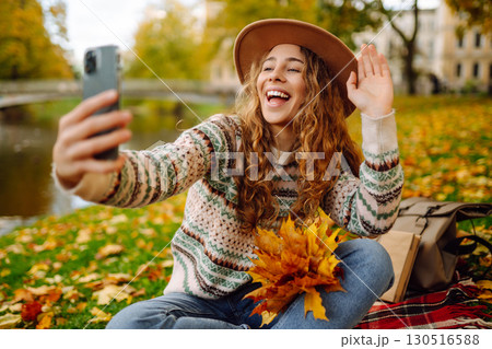 Stylish woman takes selfie on phone in autumn forest, communicates via video call. Concept of nature 130516588