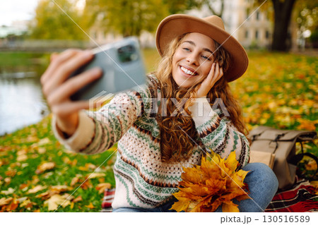 Stylish woman takes selfie on phone in autumn forest, communicates via video call. Concept of nature Stylish woman takes selfie on phone in autumn forest, communicates via video call. Concept of nature 130516589