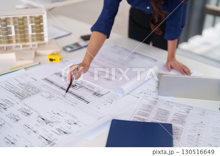 Adult Asian woman hand examines detailed architectural blueprints design plans for construction project planning development in professional office studio Adult Asian woman hand examines detailed architectural blueprints design plans for construction project planning development in professional office studio 130516649