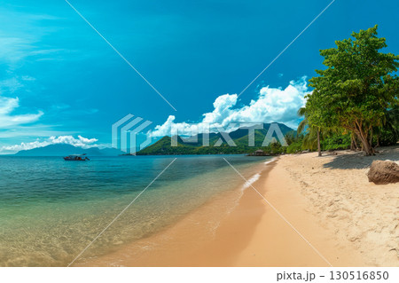 Vibrant tropical beach with golden sand, clear blue ocean, and green mountains. A small boat floats peacefully under a sunny sky with clouds. 130516850