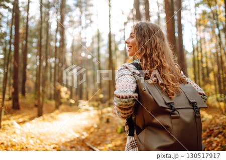Beautiful young tourist with a backpack is having fun in the autumn forest, throwing fallen leaves. Beautiful young tourist with a backpack is having fun in the autumn forest, throwing fallen leaves. 130517917