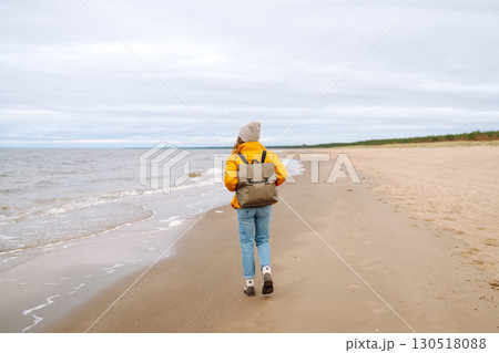 Attractive woman on windy cold beach. Beautiful tourist woman in stylish clothes enjoys life by sea. Attractive woman on windy cold beach. Beautiful tourist woman in stylish clothes enjoys life by sea. 130518088