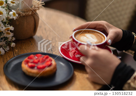 Coffee Dessert Cafe: Woman holds latte with strawberry tart and daisies at cafe in daytime to relax. 130518232