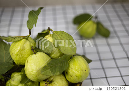 Green Guava In The Bamboo Basket On The Table, Green guavas rest fresh in a rustic bamboo basket on a wooden table, perfect for promoting organic fruit market products. 130521801
