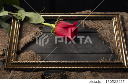 In a beautiful frame, pieces of canvas and a red rose on a wooden background. In a beautiful frame, pieces of canvas and a red rose on a wooden background. 130522425