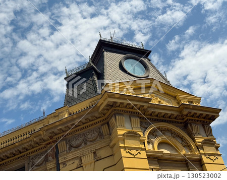 Historic tower with round clock and detailed architectural ornaments against bright sky. Heritage, culture, and urban landmark representing city tradition, design, and architectural history. Historic tower with round clock and detailed architectural ornaments against bright sky. Heritage, culture, and urban landmark representing city tradition, design, and architectural history. 130523002