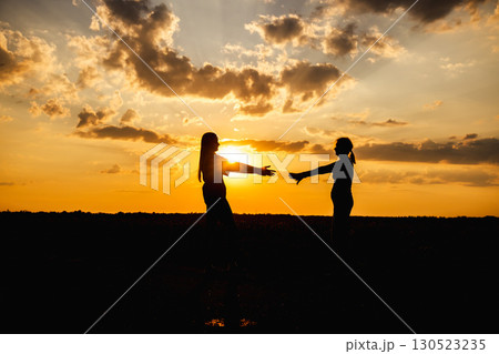 Silhouette of two women reaching out to embrace each other at sunset Silhouette of two women reaching out to embrace each other at sunset 130523235