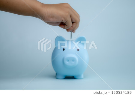 A hand is dropping coins into a piggy bank. The concept of saving and investing. A hand is dropping coins into a piggy bank. The concept of saving and investing. 130524189