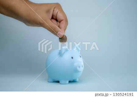 A hand is dropping coins into a piggy bank. The concept of saving and investing. 130524191