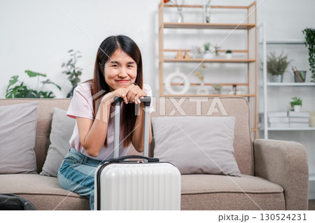 Smiling woman sitting on a sofa with a suitcase, surrounded by modern decor and plants, ready for travel. 130524231