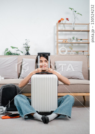 Smiling woman sitting with suitcase in cozy living room, preparing for a travel journey. Casual and relaxed atmosphere. Smiling woman sitting with suitcase in cozy living room, preparing for a travel journey. Casual and relaxed atmosphere. 130524232