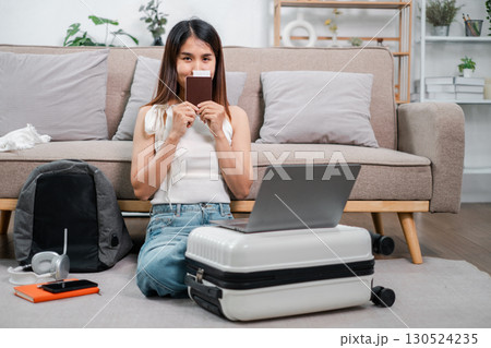 Woman sitting on floor with laptop, passport, and suitcase, ready for travel in a cozy living room. Woman sitting on floor with laptop, passport, and suitcase, ready for travel in a cozy living room. 130524235