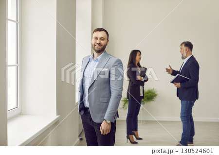 Happy smiling man looking at camera with realtor showing apartment on background. Happy smiling man looking at camera with realtor showing apartment on background. 130524601