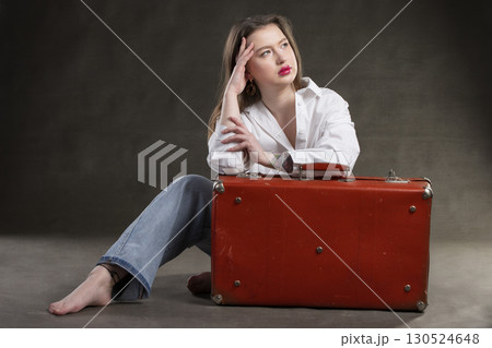 Beautiful girl sits with a vintage suitcase on a gray background. 130524648