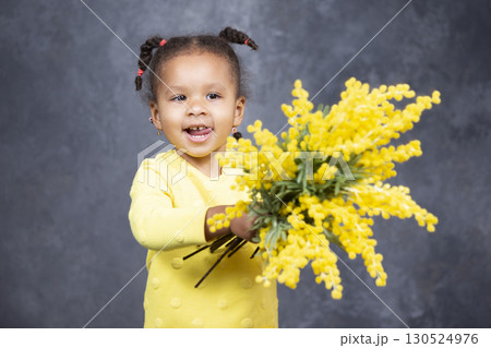 Little African American girl with yellow flowers on a gray background. 130524976