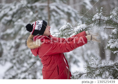 Happy middle-aged woman stands near a snow-covered Christmas tree. An adult woman on a walk in the winter forest. Happy middle-aged woman stands near a snow-covered Christmas tree. An adult woman on a walk in the winter forest. 130525439