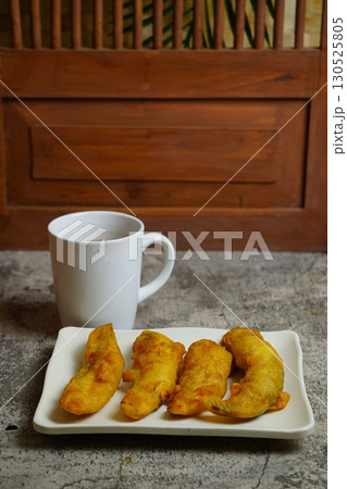 Close-up of freshly Pisang Goreng or fried Indonesian banana fritters on a white plate. A popular sweet snack or dessert. Close-up of freshly Pisang Goreng or fried Indonesian banana fritters on a white plate. A popular sweet snack or dessert. 130525805