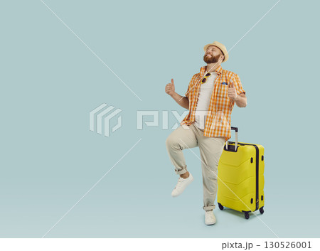 Funny young happy man in beach hat with yellow suitcase isolated on studio blue background. Funny young happy man in beach hat with yellow suitcase isolated on studio blue background. 130526001