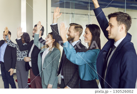 Young cheerful company employees raising hands to vote at the conference standing in meeting room. 130526002
