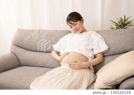 ソファーに座ってお腹をさする妊娠8ヶ月の女性 130526139