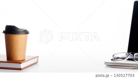 Closeup of an office table featuring a sleek laptop, a coffee cup, and reading glasses on a clean white surface 130527703