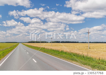 Endless asphalt road stretching through a summer landscape of green fields under a sunny sky Endless asphalt road stretching through a summer landscape of green fields under a sunny sky 130527768