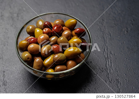 An assortment of various olives presented in a bowl, showcasing different colors, textures, and flavors 130527864
