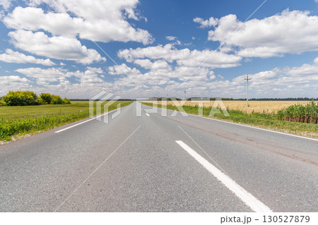 Endless asphalt road stretching through a summer landscape of green fields under a sunny sky Endless asphalt road stretching through a summer landscape of green fields under a sunny sky 130527879