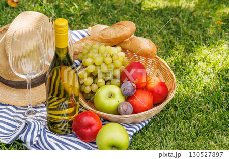 Picnic with wine, fruits, and baguette on a green meadow 130527897