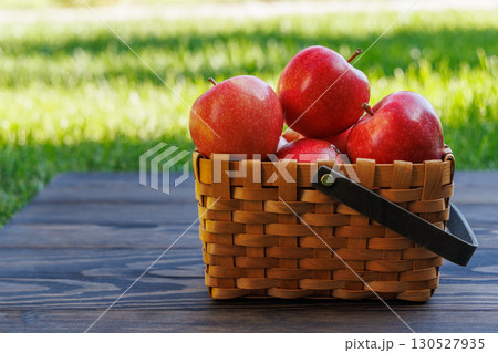 Basket of ripe red apples on a green meadow Basket of ripe red apples on a green meadow 130527935