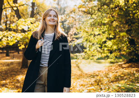 Young 30s blonde woman in coat smiling at the autumn park. Lifestyle, fashion, people and relax concept. 130528823