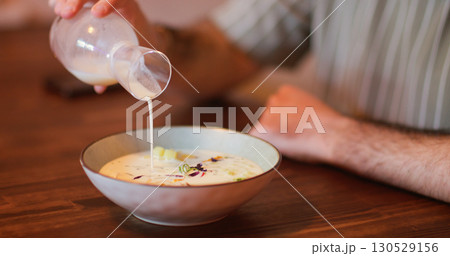 Pouring food. Cold soup. Man hand adding white liquid from glass bottle to colorful vegetable bowl. Vegetarian meal serving on table. Pouring food. Cold soup. Man hand adding white liquid from glass bottle to colorful vegetable bowl. Vegetarian meal serving on table. 130529156