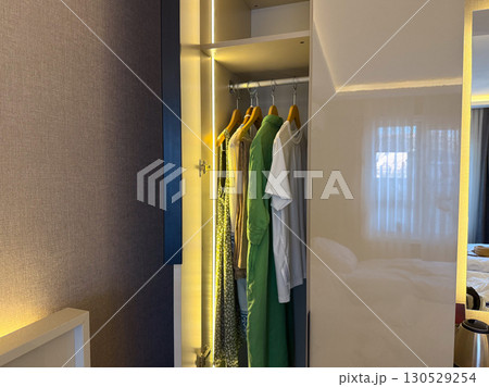Wardrobe with hanging clothes including shirts and dresses on wooden hangers. Interior design, fashion lifestyle, and daily organization in modern living space. Wardrobe with hanging clothes including shirts and dresses on wooden hangers. Interior design, fashion lifestyle, and daily organization in modern living space. 130529254