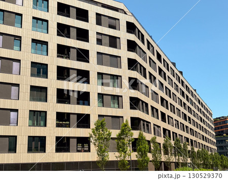 Close-up of modern apartment block facade with balconies and windows under blue sky. Contemporary architecture, housing development, and urban lifestyle symbolizing residential investment. 130529370