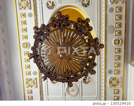 Large bronze chandelier with multiple candle-shaped bulbs in ornate ceiling interior. Architecture, tradition, and heritage design symbolizing luxury, culture, and historic decorative craftsmanship. 130529410