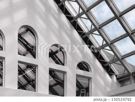 Interior view of a modern building with arched windows and a glass roof structure. Natural light 130529792
