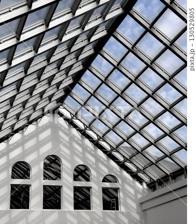 Modern architectural interior with a large geometric glass ceiling that lets sunlight stream in, 130529805