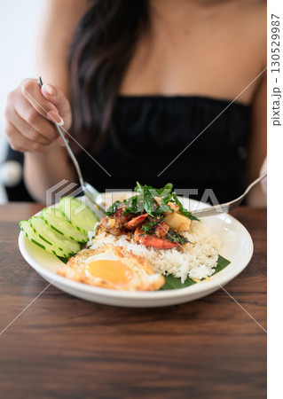 Close-up of woman in restaurant eating Thai holy basil seafood dish with fried egg and rice 130529987