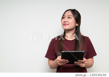 Studio portrait of young Asian woman using digital tablet computer while thinking and looking up Studio portrait of young Asian woman using digital tablet computer while thinking and looking up 130530230