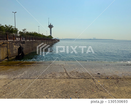 Concrete pier stretching into the sea with a tall tower visible in the background. Architecture, infrastructure, and urban coastline environment in perspective view. Concrete pier stretching into the sea with a tall tower visible in the background. Architecture, infrastructure, and urban coastline environment in perspective view. 130530693
