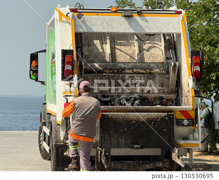 Worker approaching a garbage truck during waste collection service. Urban labor, transportation, and environmental management in city infrastructure. Worker approaching a garbage truck during waste collection service. Urban labor, transportation, and environmental management in city infrastructure. 130530695
