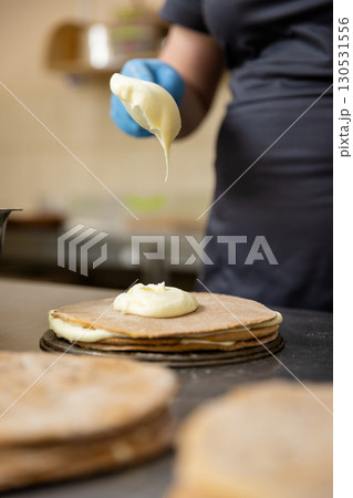 Pastry chef spreading cream on cake layer in professional bakery kitchen, close-up 130531556