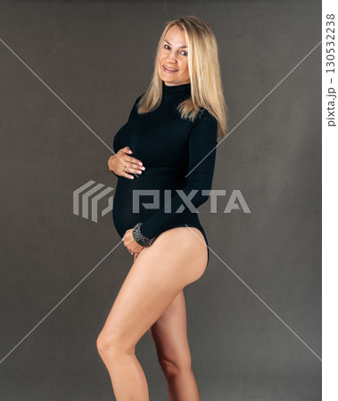 Pregnant woman in a black bodysuit gently holds her belly, showcasing a calm and joyful expression. The image captures the beauty and joy of pregnancy in a studio setting. 20 week Pregnant woman in a black bodysuit gently holds her belly, showcasing a calm and joyful expression. The image captures the beauty and joy of pregnancy in a studio setting. 20 week 130532238