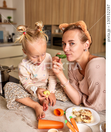 Mother and daughter enjoy cooking and playful bonding time in a cozy kitchen 130532297